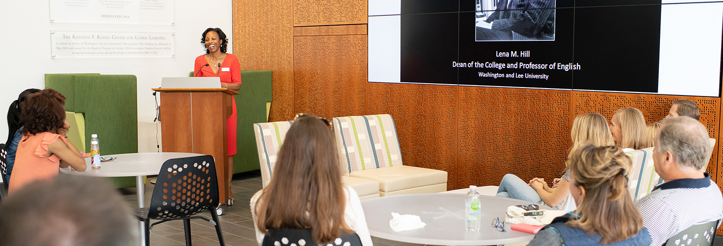Dean Lena Hill uses the atrium display screen to give a presentation before an audience.